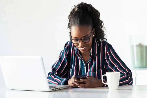 Досить молода бізнес-леді, використовуючи свій смартфон під час роботи з ноутбуком в офісі . — стокове фото