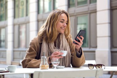 Bir kahve dükkanının terasında kahve içerken onun cep telefonu kullanarak Pretty genç kadın.