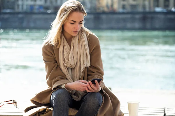 Mooie jonge vrouw met behulp van haar mobiele telefoon naast de rivier in de stad. — Stockfoto