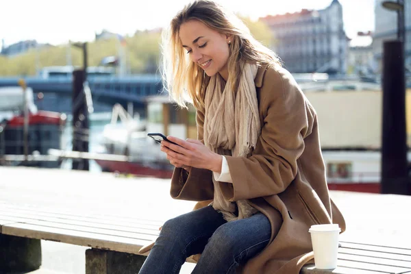 Hermosa joven usando su teléfono móvil al lado del río en la ciudad . — Foto de Stock