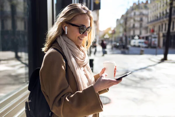 Mooie jonge vrouw luisteren naar muziek met draadloze koptelefoon en de smartphone in de straat. — Stockfoto