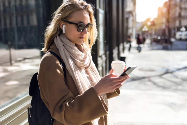 Mooie jonge vrouw luisteren naar muziek met draadloze koptelefoon en de smartphone in de straat. — Stockfoto