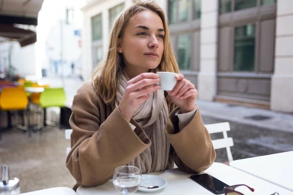 Mulher bonita olhando para o lado enquanto bebe uma xícara de café no terraço de um café . — Fotografia de Stock