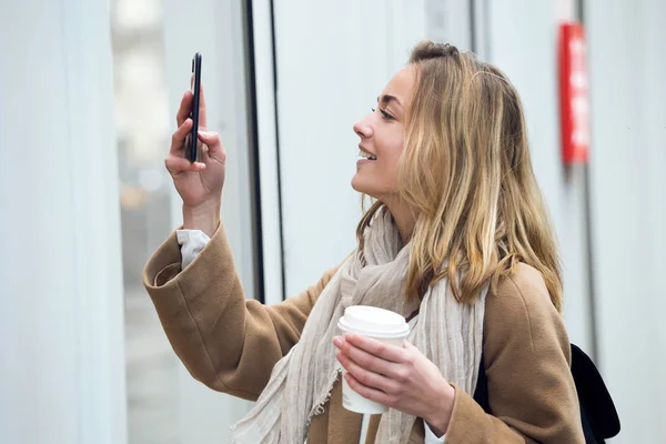 Hermosa joven mujer haciendo fotos de un escaparate con móvil en la calle . —  Fotos de Stock