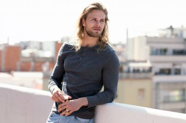 Evde çatıda şişe bira içerken yakışıklı genç adam yan bakıyor.