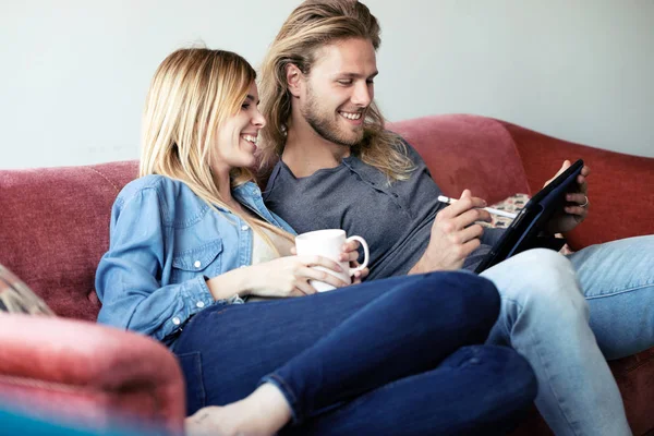 Schönes junges Paar zeichnet mit dem digitalen Tablet, während es zu Hause auf dem Sofa sitzt. — Stockfoto