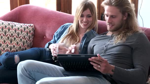 Schönes junges Paar zeichnet mit dem digitalen Tablet, während es zu Hause auf dem Sofa sitzt. — Stockvideo