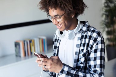 Yakışıklı genç afro-amerikan adam evde cep telefonu kullanırken gülümseyen.