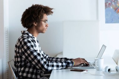 Ofiste dizüstü bilgisayarını kullanarak gözlüklü genç Afro-Amerikan adam konsantre.