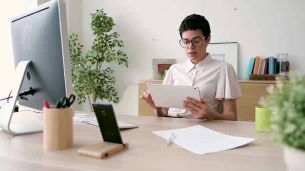 オフィスで働きながらデジタルタブレットを使って笑顔の若いビジネスウーマンの動画 — ストック動画
