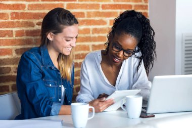 Ofiste dijital tablet ile birlikte çalışan iki güzel genç iş kadını.