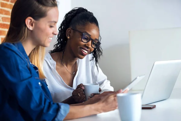 Dos mujeres de negocios bastante jóvenes trabajando junto con la tableta digital en la oficina . — Foto de Stock