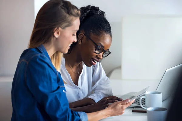 Deux jolies jeunes femmes d'affaires qui travaillent ensemble avec une tablette numérique au bureau . — Photo