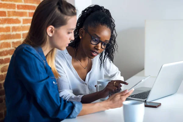 Deux jolies jeunes femmes d'affaires qui travaillent ensemble avec une tablette numérique au bureau . — Photo