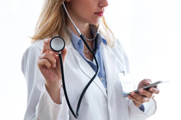 Médica feminina segurando estetoscópio e usando seu smartphone sobre fundo branco . — Fotografia de Stock