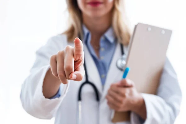 Jonge vrouw arts het selecteren van iets blanco met de vinger naar de camera over witte achtergrond. — Stockfoto