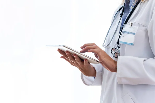 흰색 배경 위에 서있는 동안 그녀의 디지털 태블릿을 사용하여 흰색 실험실 코트에 여성 의사. — 스톡 사진