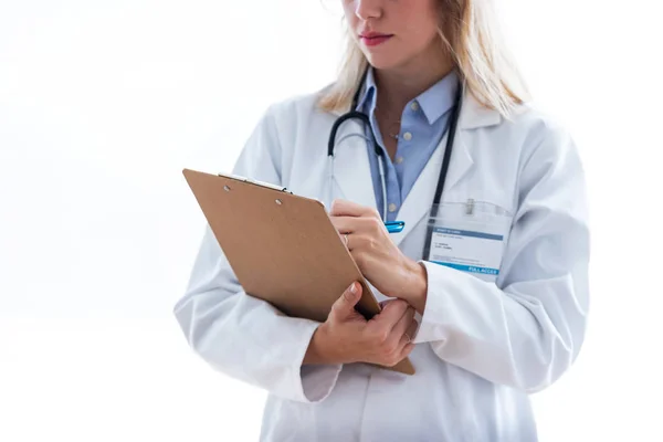 Femmina medico riempiendo modulo medico negli appunti mentre in piedi dritto su sfondo bianco . — Foto Stock