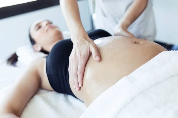 Fisioterapeuta femenina masajeando barriga en mujer embarazada en centro de spa . — Foto de Stock