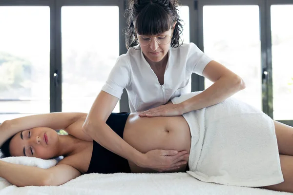 Fisioterapeuta femenina masajeando barriga en mujer embarazada en centro de spa . — Foto de Stock