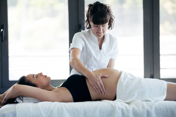 Female physiotherapist massaging tummy on pregnant woman in spa center. — Stock Photo, Image