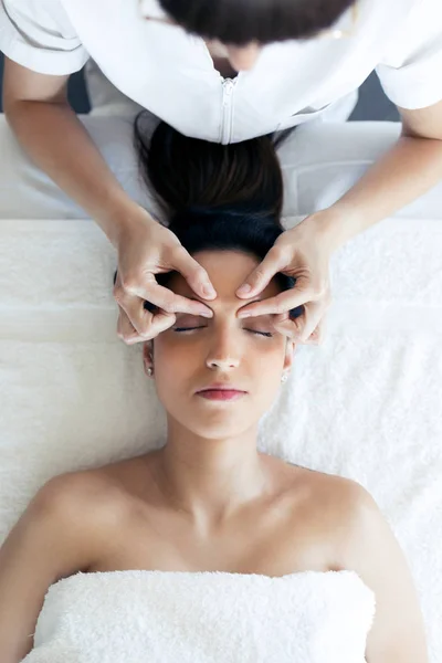 Masajista haciendo masaje facial terapéutico a joven embarazada en centro de spa . — Foto de Stock