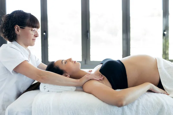 Fisioterapeuta masajeando los hombros de la mujer embarazada en el centro de spa . — Foto de Stock