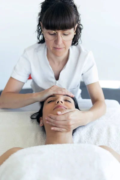 Masajista haciendo masaje facial terapéutico a joven embarazada en centro de spa . — Foto de Stock