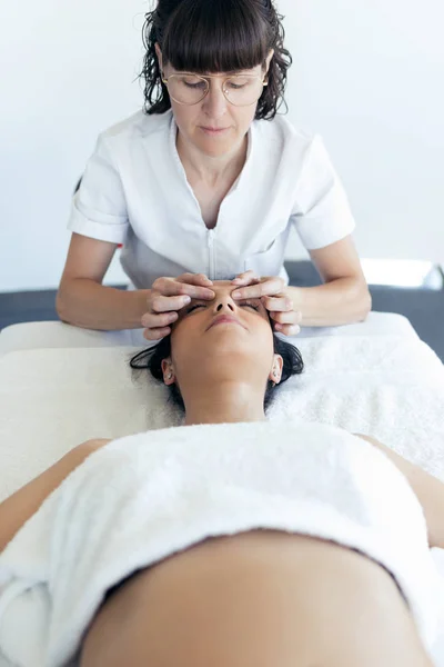 Masajista haciendo masaje facial terapéutico a joven embarazada en centro de spa . — Foto de Stock