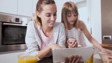 Evde mutfakta kahvaltı yaparken dijital tablet kullanarak Pretty genç anne ve kızı.
