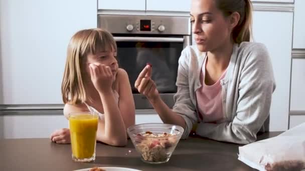 Hermosa madre y su hija tomando y comiendo cereales de tazón en la cocina en casa . — Vídeos de Stock