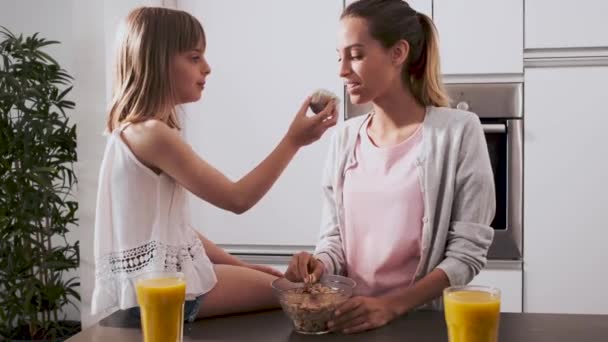 Mooie jonge moeder en haar dochter genieten van tijd terwijl het eten van ontbijt in de keuken thuis. — Stockvideo