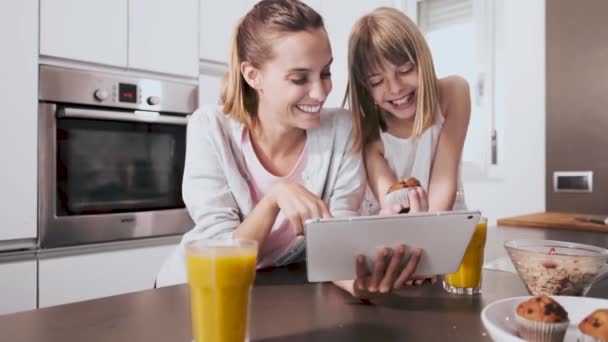 自宅の台所で朝食を食べながら、かなり若い母親と彼女の娘は、デジタルタブレットを使用して. — ストック動画