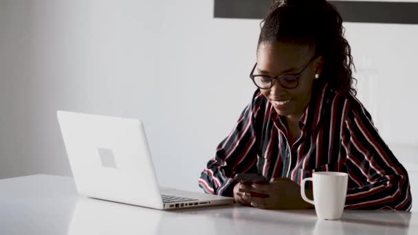 Jolie jeune femme d'affaires utilisant son smartphone tout en travaillant avec un ordinateur portable dans le bureau . — Video