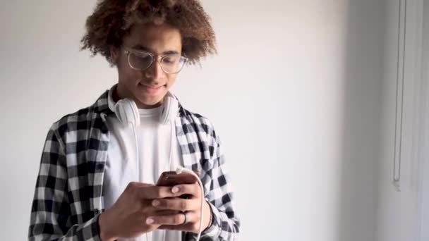 Knappe jonge Afro-Amerikaanse man die zijn mobiele telefoon thuis gebruikt. Geïsoleerd op witte achtergrond. — Stockvideo