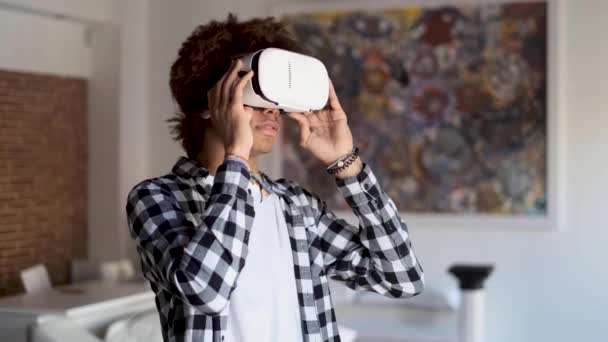 Ευτυχισμένος Αφρο-Αμερικανός νέος άνθρωπος χρησιμοποιώντας τα γυαλιά εικονικής πραγματικότητας του, ενώ στέκεται στο σπίτι. — Αρχείο Βίντεο