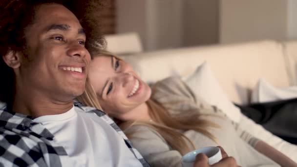 Щаслива молода пара дивиться телевізор разом, сидячи на дивані вдома . — стокове відео