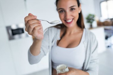 Güzel genç kadın evde yoğurt yerken kameraya arıyor.