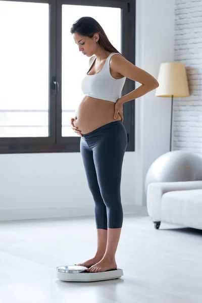 Preocupado embarazada joven de pie en la balanza en casa . —  Fotos de Stock