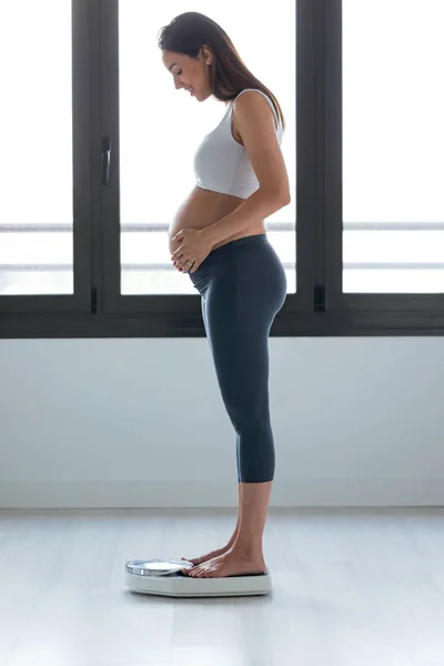Bastante joven embarazada de pie en la balanza en casa . —  Fotos de Stock