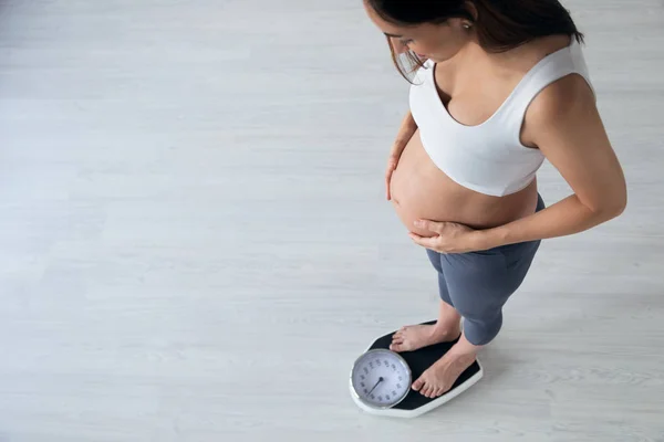 Mooie jonge zwangere vrouw staand op schubben thuis. — Stockfoto