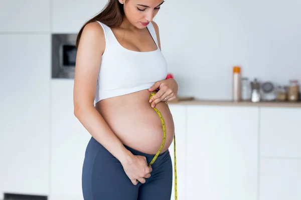 Mooie zwangere vrouw die haar buik meet met een tape om de ontwikkeling van haar foetus bij te houden. Gezond zwangerschaps concept. — Stockfoto