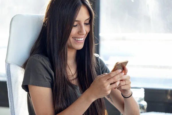 Lächelnde junge Geschäftsfrau, die im Büro Nachrichten mit dem Handy verschickt. — Stockfoto