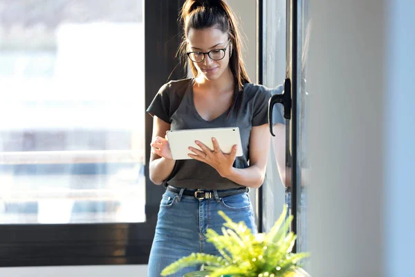 Leende ung affärskvinna med sin digitala tablett stående bredvid fönstret på kontoret. — Stockfoto