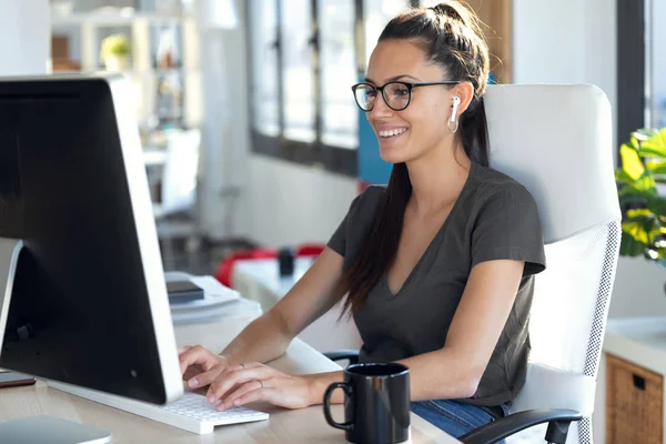 Sourire jeune femme d'affaires travaillant avec son ordinateur tout en écoutant de la musique au bureau . — Photo