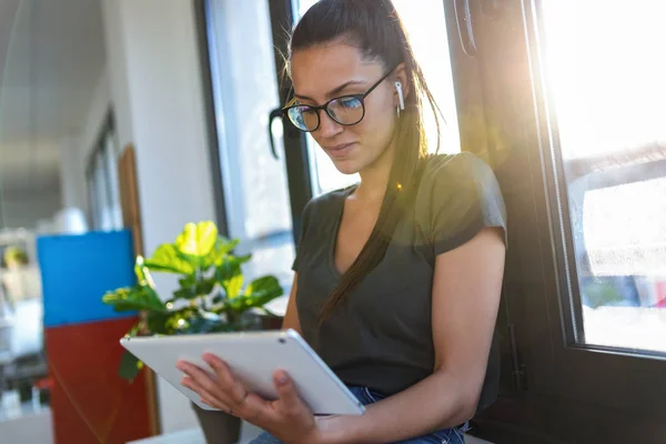 Joven mujer de negocios sonriente usando su tableta digital mientras está sentada junto a la ventana de la oficina . —  Fotos de Stock