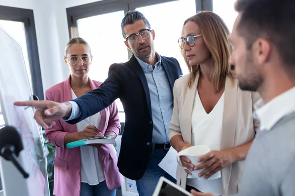 Hombre de negocios guapo apuntando a pizarra blanca y explicar un proyecto a sus colegas en el lugar de coworking . — Foto de Stock