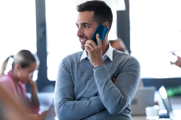 Smiling young businessman talking on mobile phone on coworking space. — Stock Photo, Image