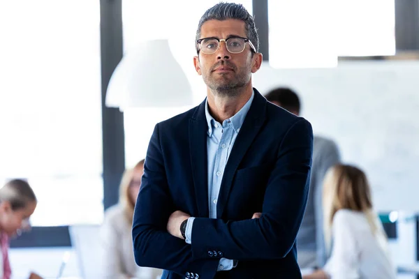 Knappe zakenman kijkt naar camera terwijl zijn collega's werken aan coworking place. — Stockfoto