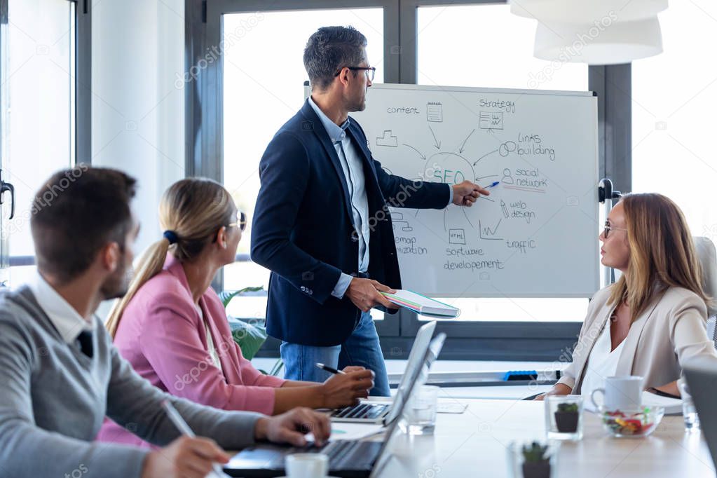 Handsome businessman pointing at white blackboard and explain a project to her colleagues on coworking place.